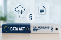 Zwei Aktenordner nebeneinander auf einem Tisch: ein dunkelblauer Ordner mit dem EU-Sternenkranz-Logo und der Aufschrift „Data Act" sowie ein hellgrauer Ordner mit der Aufschrift „Durchführungsgesetz" und einem Paragrafenzeichen. Darüber grafische Icons: eine Cloud mit Pfeilen (Datentransfer), ein Paragrafenzeichen in einem Kreis und ein Dokumentensymbol, verbunden durch gestrichelte Linien.